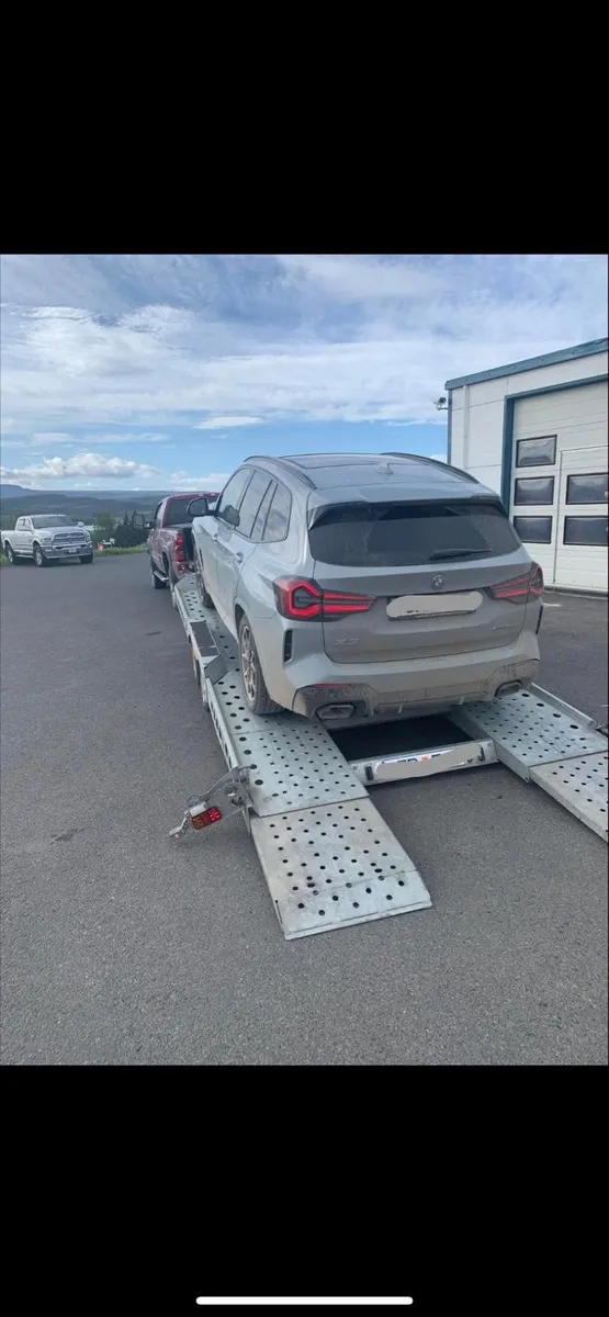 BMW X3 on a vehicle transport trailer outside a garage